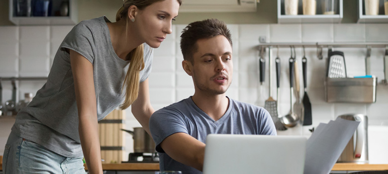 Couple looking at bills in front of laptop at kitchen table